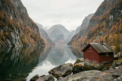 Paysage de fjord norvégien en automne avec cabane en bois rouge et eaux calmes reflétant les falaises rocheuses